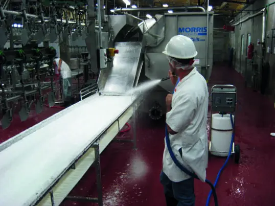 Worker cleaning industrial equipment with hose.