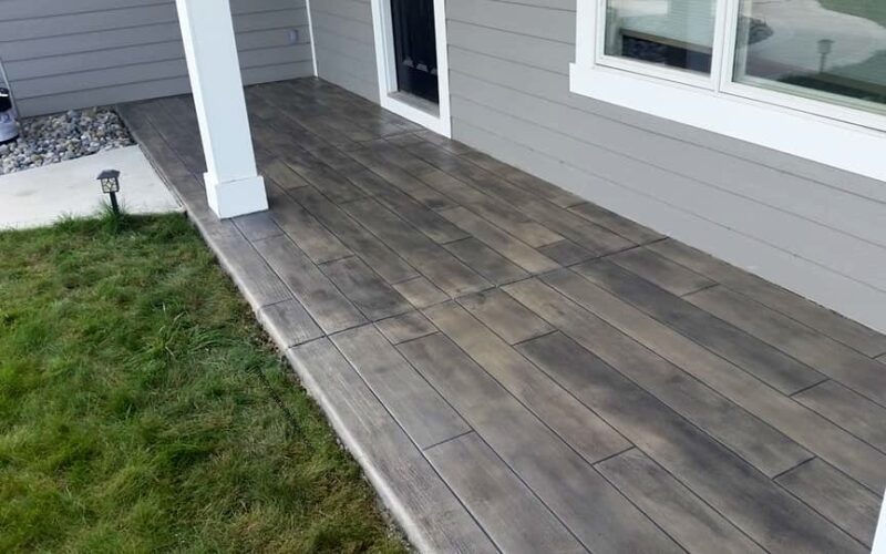 Wooden porch with grass and gray siding.
