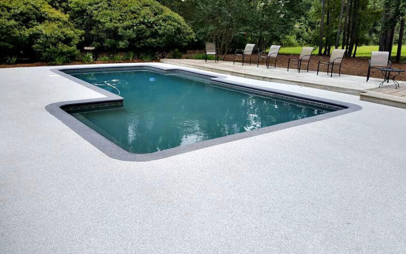 Rectangular pool with surrounding chairs and trees.